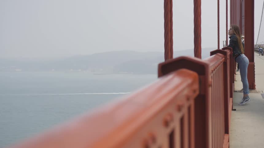 A caucasian female is on a bridge looking at the water