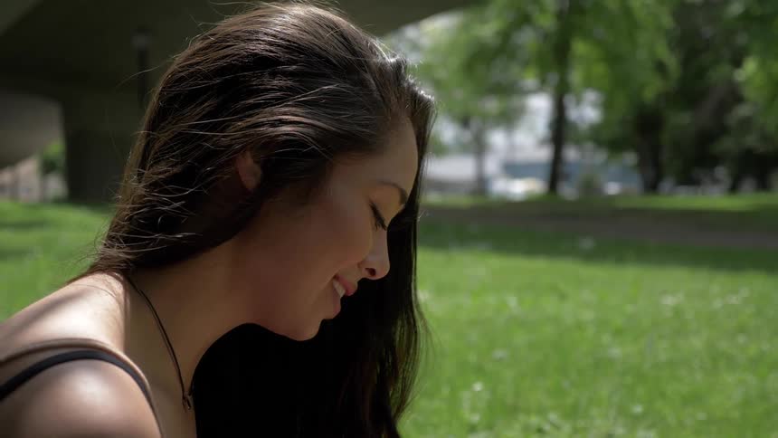 A woman sitting in the grass looks down and smiles on a sunny day