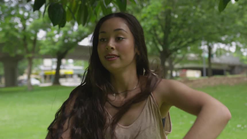 A woman with long hair dances beneath a tree in a park