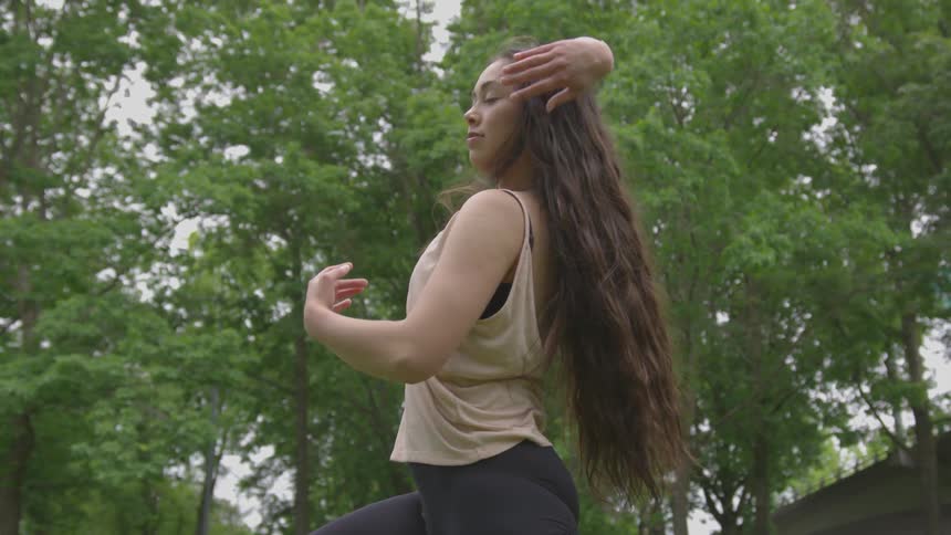 A young brunette dances under green trees