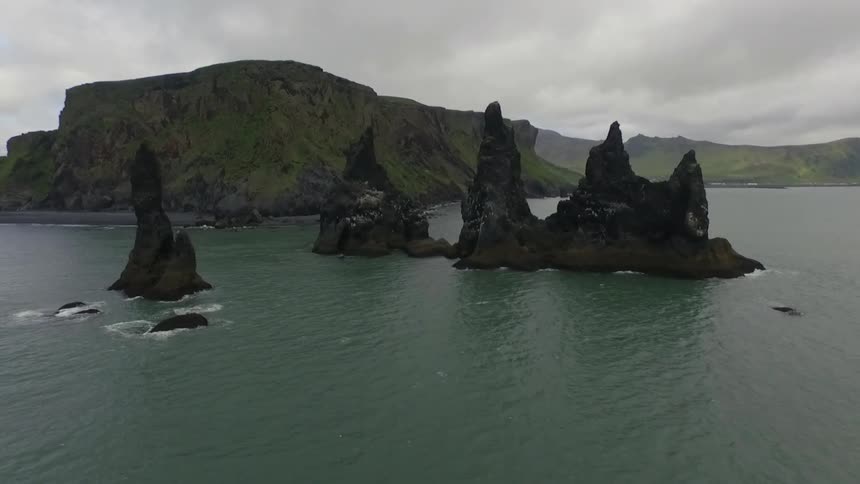 Large rock formations sit in the water next to green cliffs