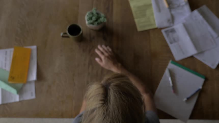 A woman sits at a table pushing opened mail away