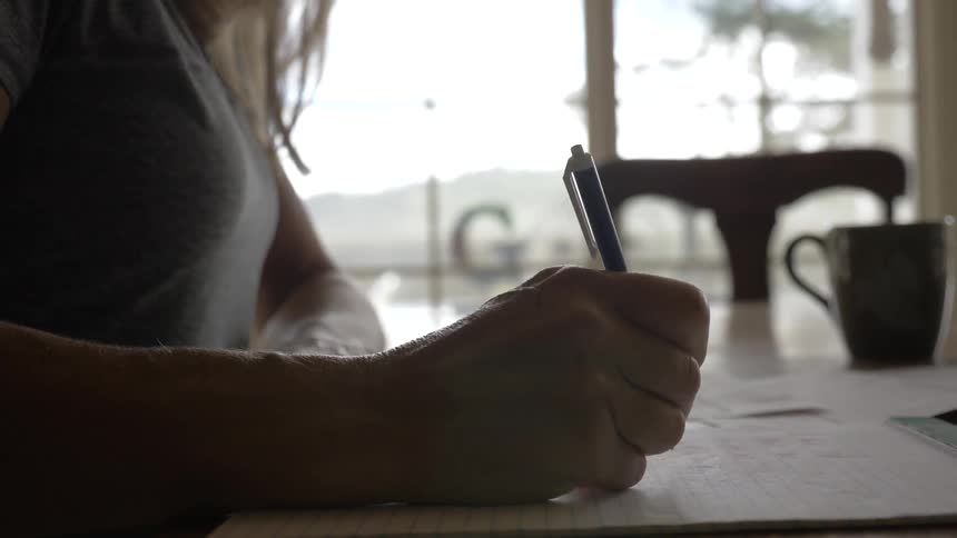 Woman sits at dining table writing in a notepad