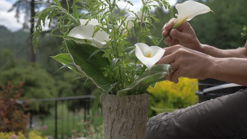 A man makes a flower arrangement while sitting on a deck or porch