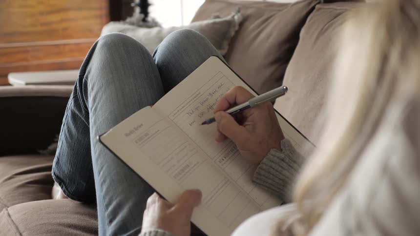 A woman sitting on a couch writing in a notebook