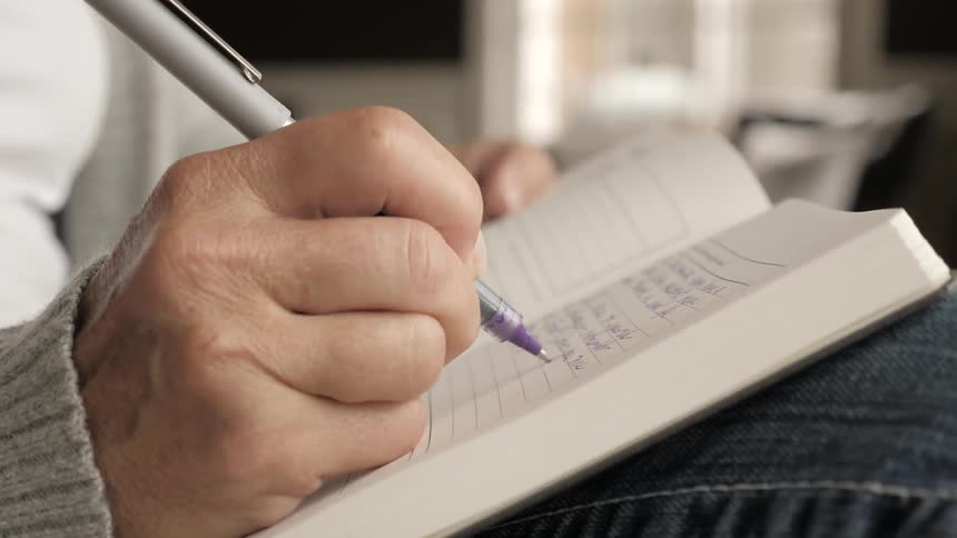 A person writes in a notebook while sitting