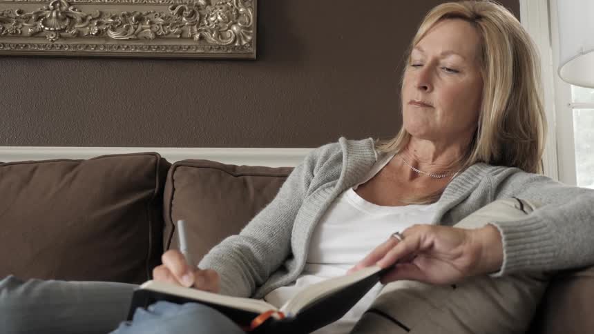 Woman sits on couch writing in journal