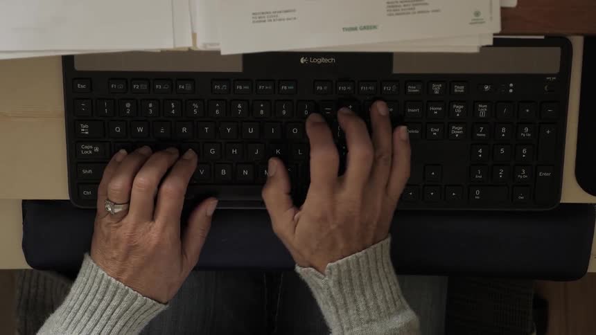 A woman types on a keyboard with a stack of papers in front
