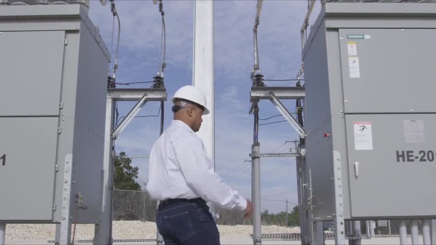 A black electrical worker in a hard hat reaching for a power box