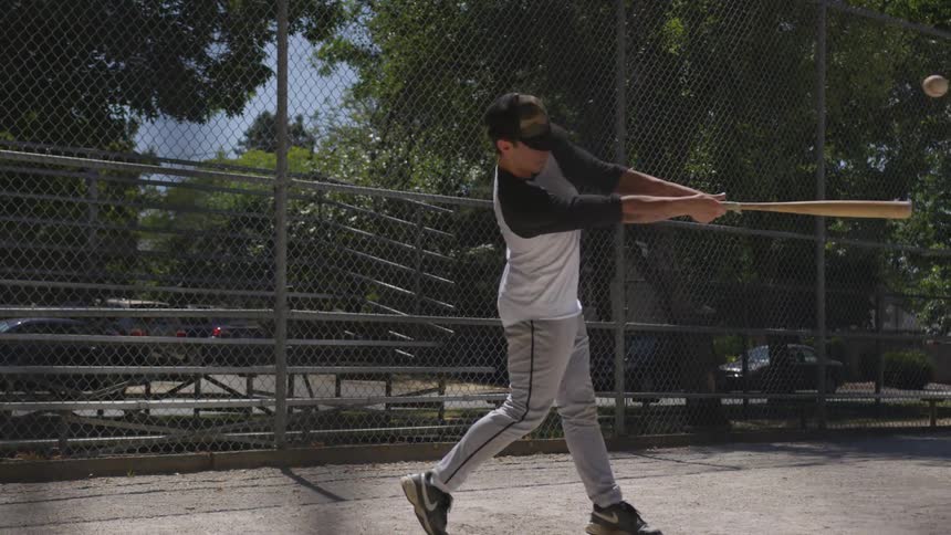 A boy tossing a baseball then hitting it with a bat