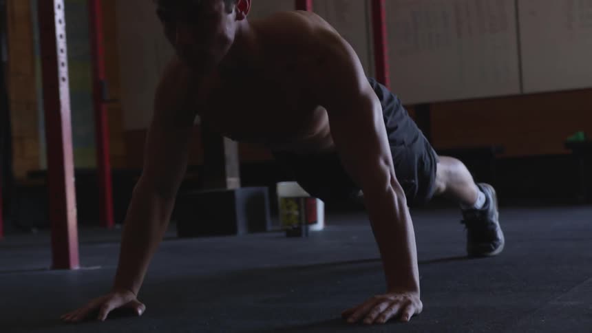 A shirtless man does push ups in a gym