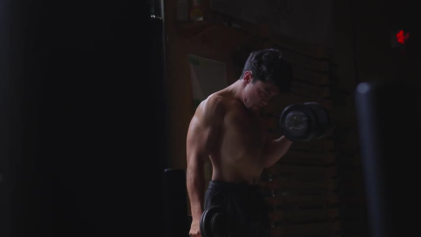 A young man lifts weights in a dark room