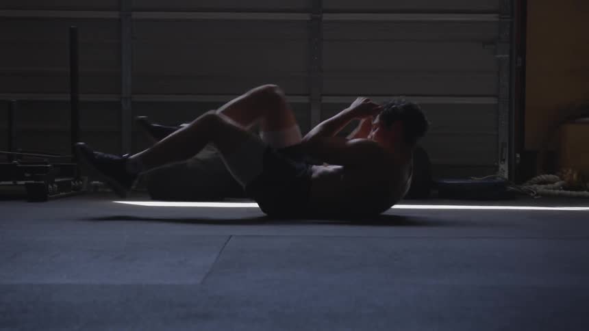 Half naked man does sit ups in a dimly lit space