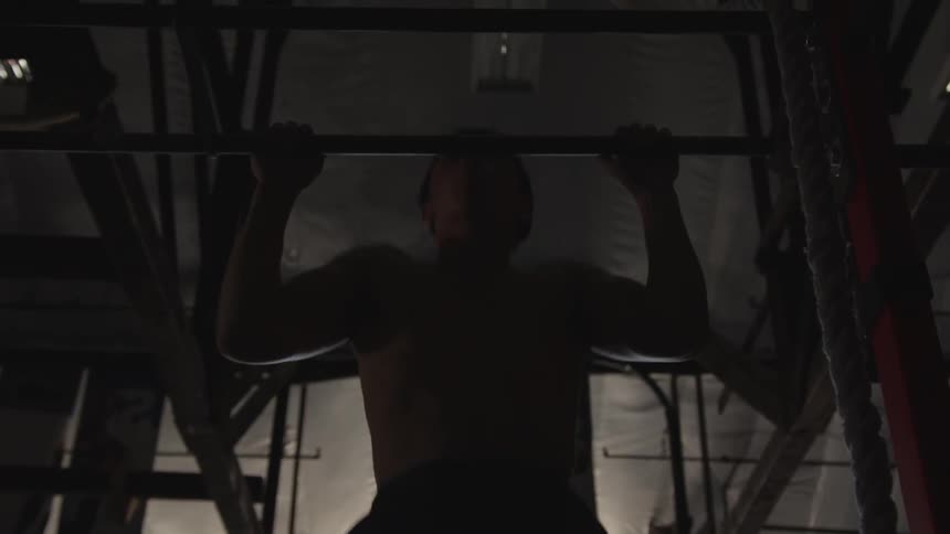 A man does pull ups in a dark gym