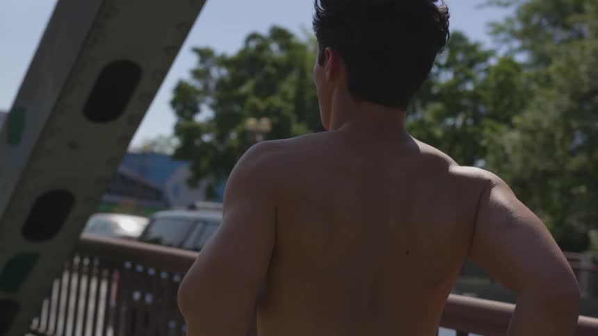A man without a shirt runs on a bridge next to traffic