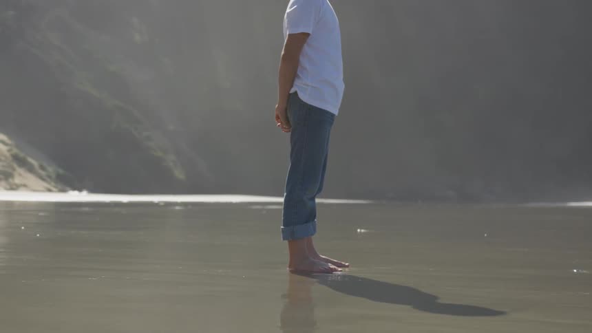A boy standing on the wet sand on the beach