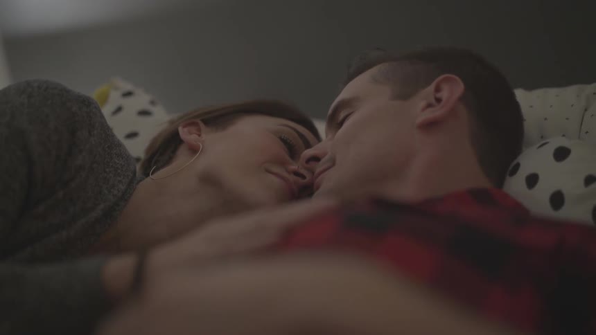 A man a woman kissing while laying on a bed