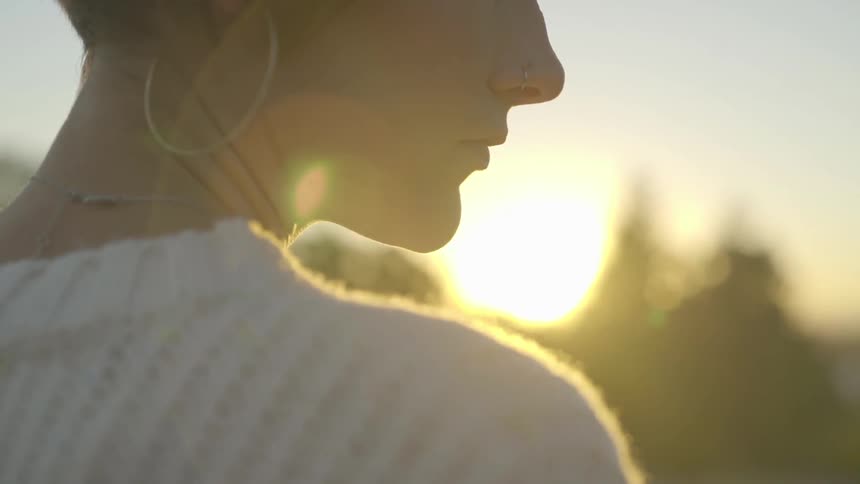 Woman looks down and to the right while outdoors at sunset