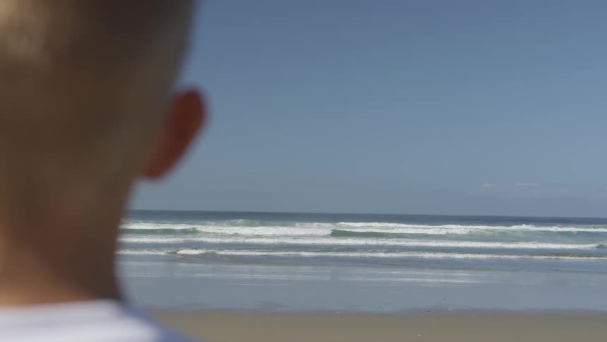 A boy standing staring at the ocean
