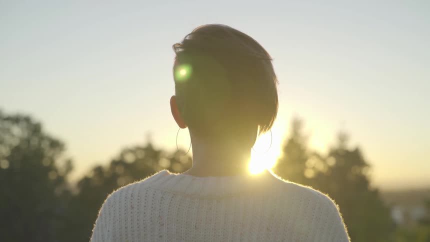 Woman stands looking at sunset