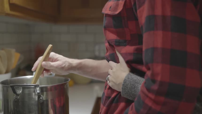 A woman hugs a man from behind as he stirs a pot on the stove
