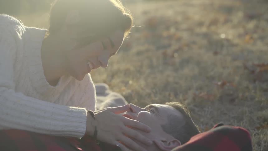 A white couple lie on the ground and smile and kiss
