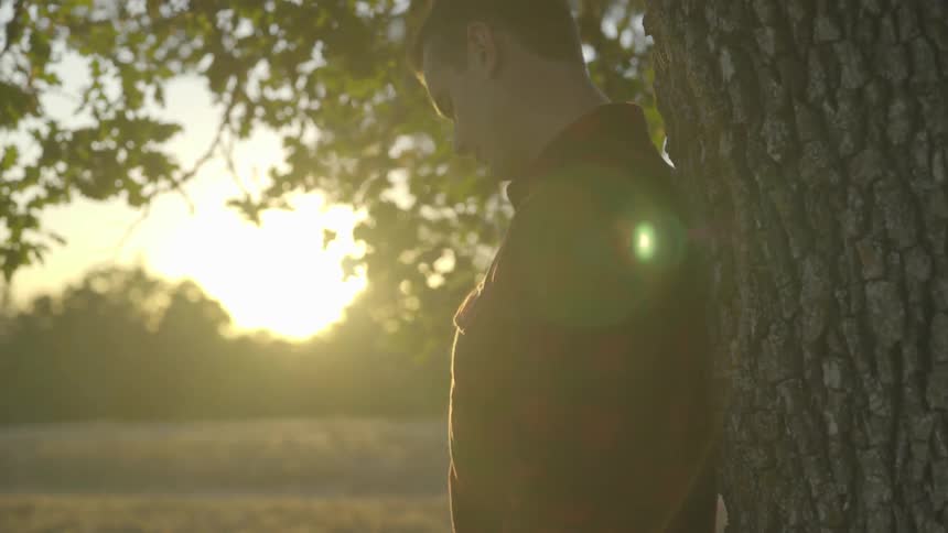 Man stands against tree in the woods at sunset