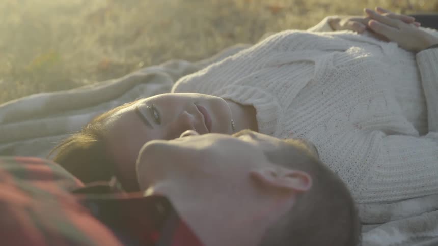 A couple lying outside on a blanket turn their heads and look at each other
