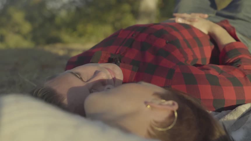 A couple lying down on a blanket in the grass turns their heads and look at each other