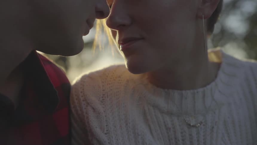 A man and woman sit and lean into each other face to face and nose to nose at sunset