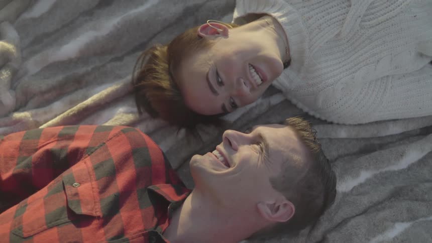 A man and a woman laughing while laying on a blanket