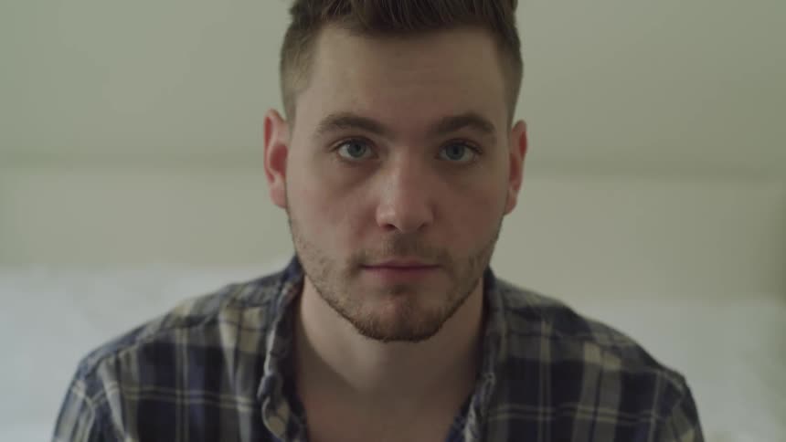 A man stares into the camera while sitting in a room