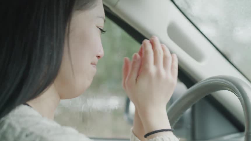 A woman holds her hands to her face and cries in her car until she hits the steering wheel in anger