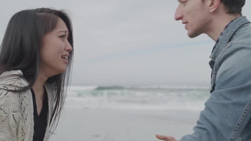 An upset man and a crying woman having a dispute on a beach