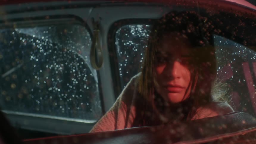 Woman looks out of a car window covered with rain