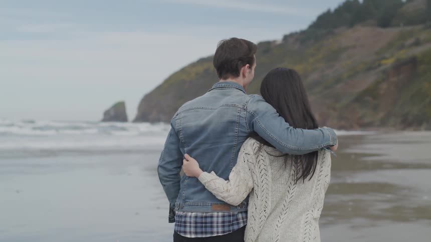 A man and a woman walking on a beach hugging
