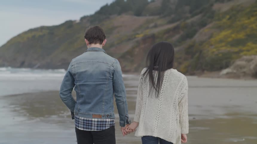 Couple walks along the beach holding hands