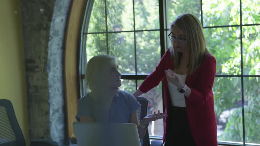 Two women have a conversation and look at the laptop in the office during daytime