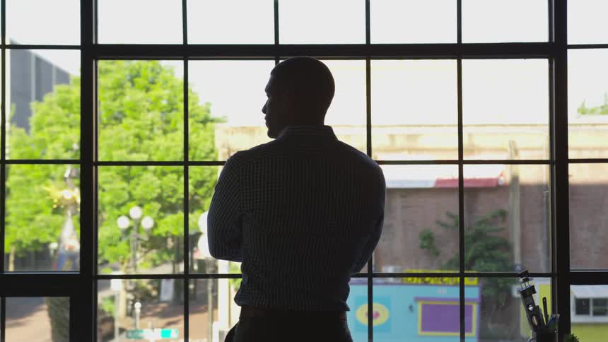 A man standing at a window with his arms folded
