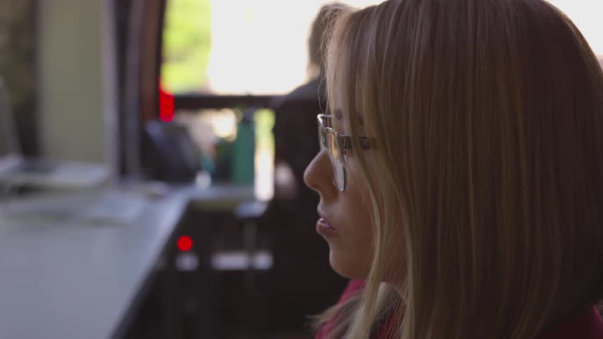Blonde woman wearing glasses sit at the table and types at the office during daylight