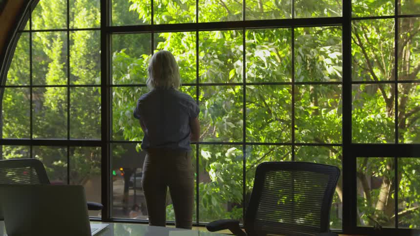 A young woman looks out the window at the trees blowing