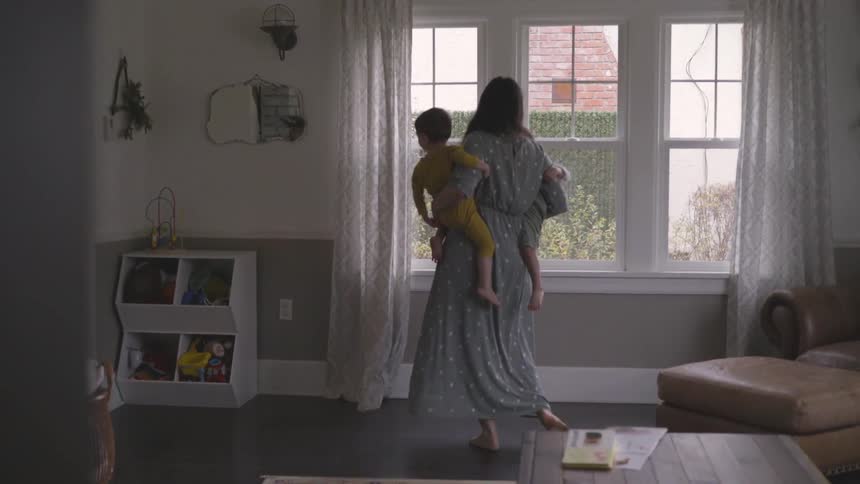 A woman holds two toddlers and sways with them by the window