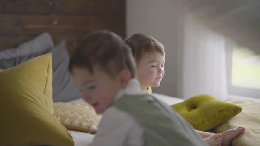 Pillows being tossed at small children playing on a bed