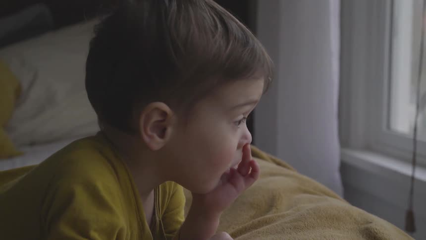 A boy laying on a bed while looking out a window