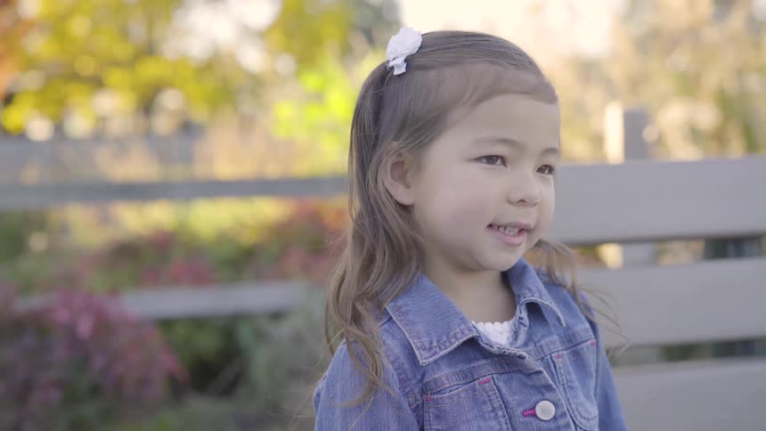 A child laughs standing beside a park bench
