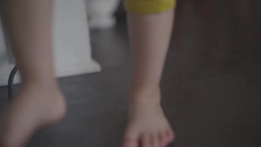 Bare feet kid stands next to the wall at house during daylight