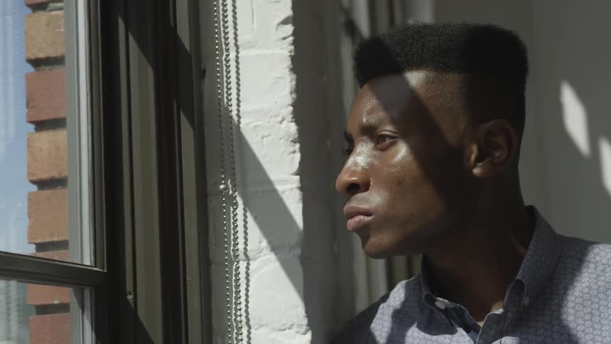 Black male looks out the window as the sun shines on his face