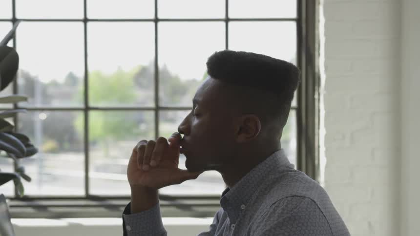 Young working professional sits with chin in hand and eyes closed in office