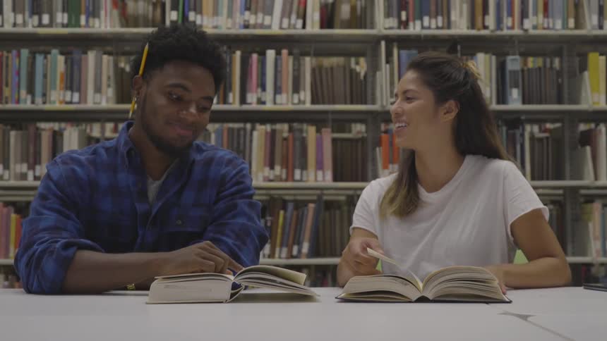 A man and a woman laugh while studying together in a library