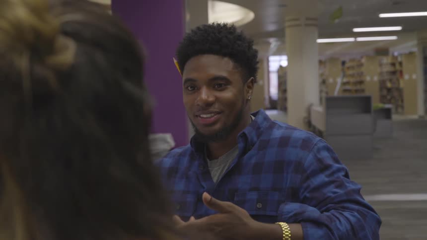 A man and woman talk while studying in a library
